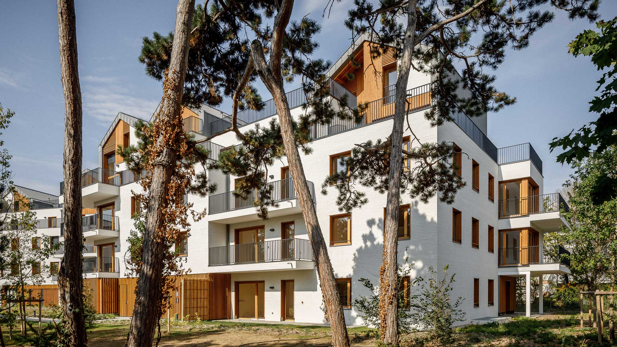 Résidence de logements collectifs au Vésinet (Yvelines), conçue par Cussac Architectes et Associés (CA+A), avec façades en briques blanches, menuiseries en bois, larges balcons et insertion dans un environnement boisé.